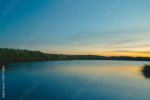 Calm peaceful lake sunset with colorful sky on background and smooth reflection on water
