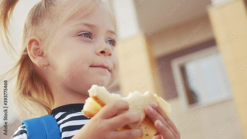 schoolgirl eating a sandwich during recess in school. kids education concept. little girl kid schoolgirl with a backpack lifestyle eating a sandwich. kid child is having lunch school