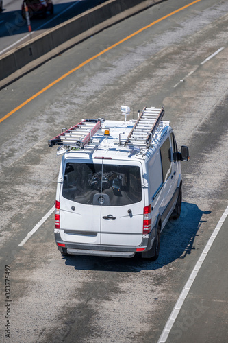 Commercial compact cargo mini van with ladders on the roof driving on the turning overpass road intersection