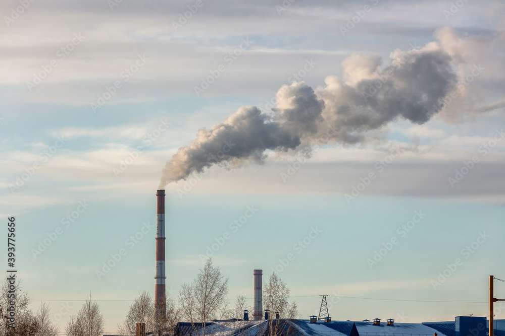 Shot of roof tops and pipes of heating plant that supply central heating system of the city. Smoke coming out of the pipes. Blue cloudy sky as a background. Industrial landscape. Barnaul, Russia