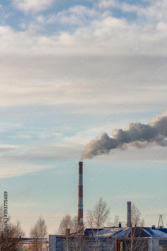 Shot of roof tops and pipes of heating plant that supply central heating system of the city. Smoke coming out of the pipes. Blue cloudy sky as a background. Industrial landscape. Barnaul, Russia