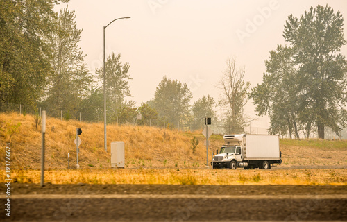 Small rig semi truck with refrigerated box trailer transporting cargo running on the road in smoke and smog from a forest fire photo