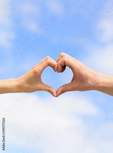 Female and man hands in the form of heart against the sky. Hands in shape of love heart. Heart from hands on a sky background
