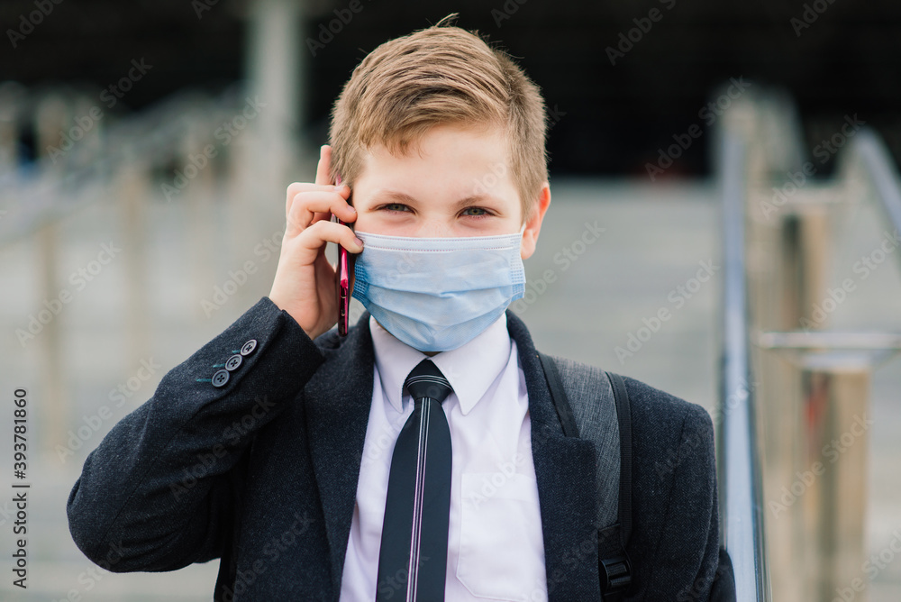 Schoolboy walks out of school wearing protective mask in a city