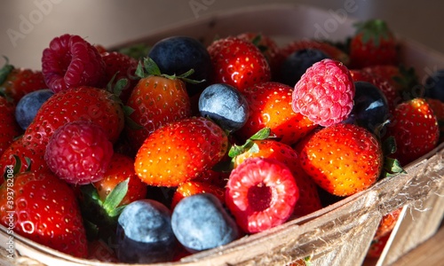  Strawberries blueberries and raspberries on a wooden tray and light background