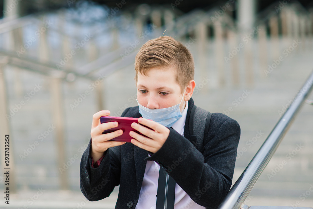 Schoolboy walks out of school wearing protective mask in a city Schoolboy walks out of school wearing protective mask in a city