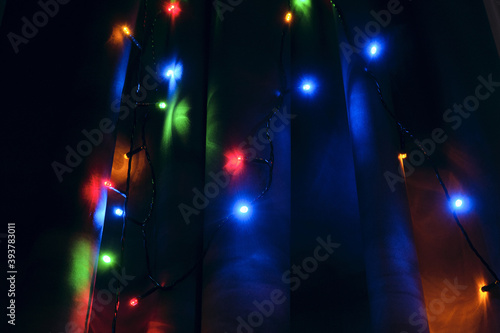 Light of a colorful Christmas home garland on the window curtain at night