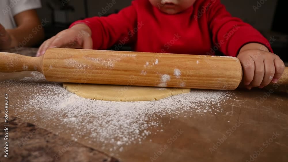 The child learns to roll the dough with a rolling pin The child learns to roll the dough with a rolling pin