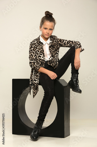 beautiful teenage girl in a spotted long jacket and black trousers sits on a black cube