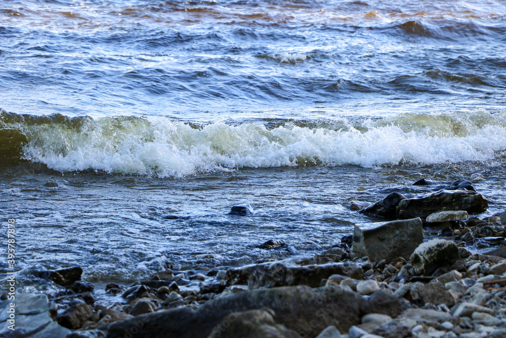 waves run onto the shore and crash against the rocks, creating many splashes and splashes near the shore. river surf in stormy weather near a stone pebble coast with foamy splashing waves. waves run onto the shore and crash against the rocks, creating many splashes and splashes near the shore. river surf in stormy weather near a stone pebble coast with foamy splashing waves.