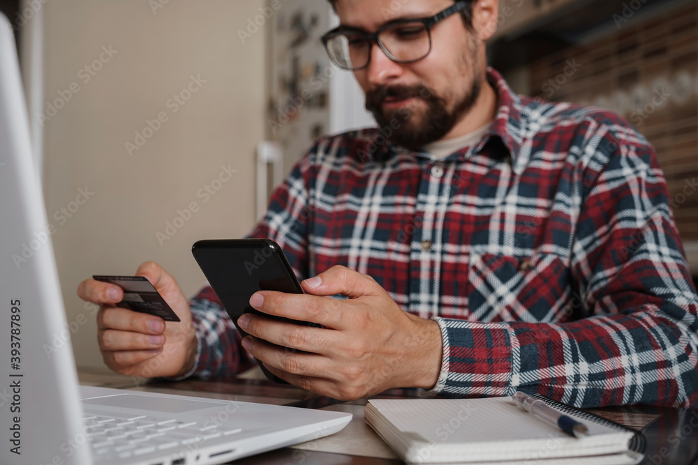 Handsome man using credit card to pay online with smartphone Handsome man using credit card to pay online with smartphone