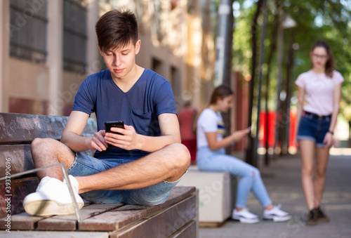 Teenager is typing message on smartphone while sitting on street bench