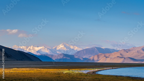 Landscape view of shore of Karakul lake at sunrise, with Muskol snow-capped mountain range in background, Murghab, Gorno-Badakshan, Tajikistan Pamir