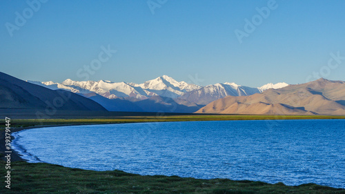 Fotografie Scenic view of Karakul lake shore at sunrise, with Muzkol snowcapped mountain ra