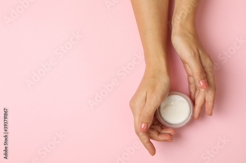 Cute female hands hold jar of cosmetic cream on pink background