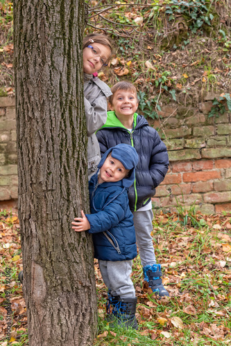 Sister and two brothers is standing next to a tree. Childrens playing in the autumn day