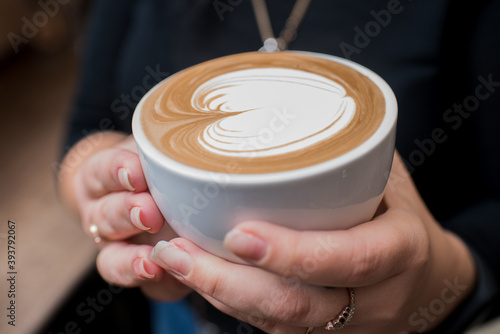 Barista girl holding fragrant freshly made cappuccino in her hands