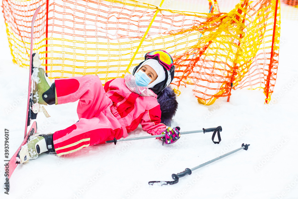 Obraz premium Portrait of a little girl skier in medical mask during COVID-19 coronavirus on a snowy mountain at a ski resort