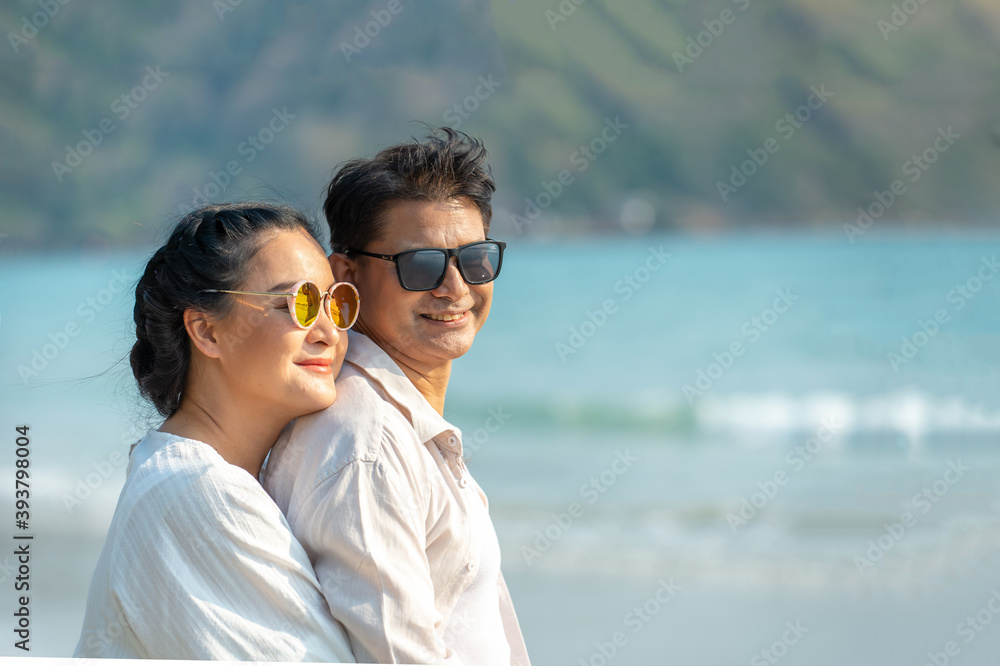 Happy Asian family senior couple hugging together on island beach and looking away to the sea with smiling face. Retirement old age people man and woman relax and enjoy summer holiday vacation