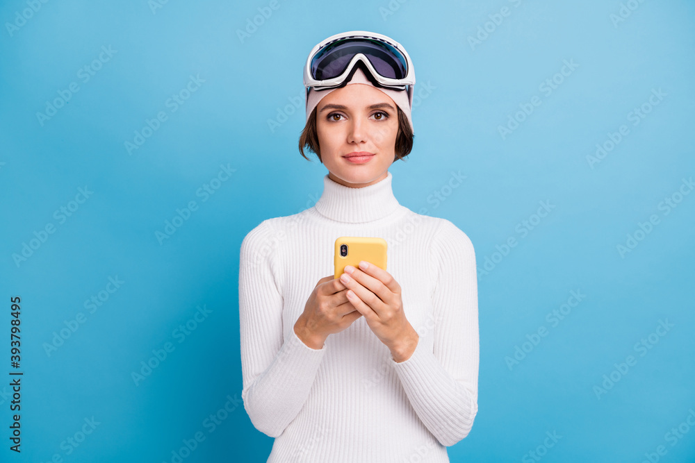Photo of brown bob haired woman hold phone wear ski gear serious mood isolated on blue color background Photo of brown bob haired woman hold phone wear ski gear serious mood isolated on blue color background