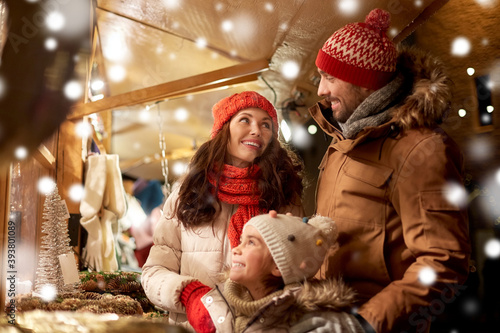 family, winter holidays and celebration concept - happy mother, father and little daughter at christmas market on town hall square in tallinn, estonia over snow