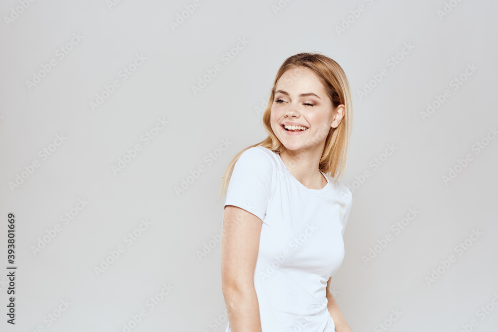 cheerful blonde in a white t-shirt gesturing with her hands light background cheerful blonde in a white t-shirt gesturing with her hands light background