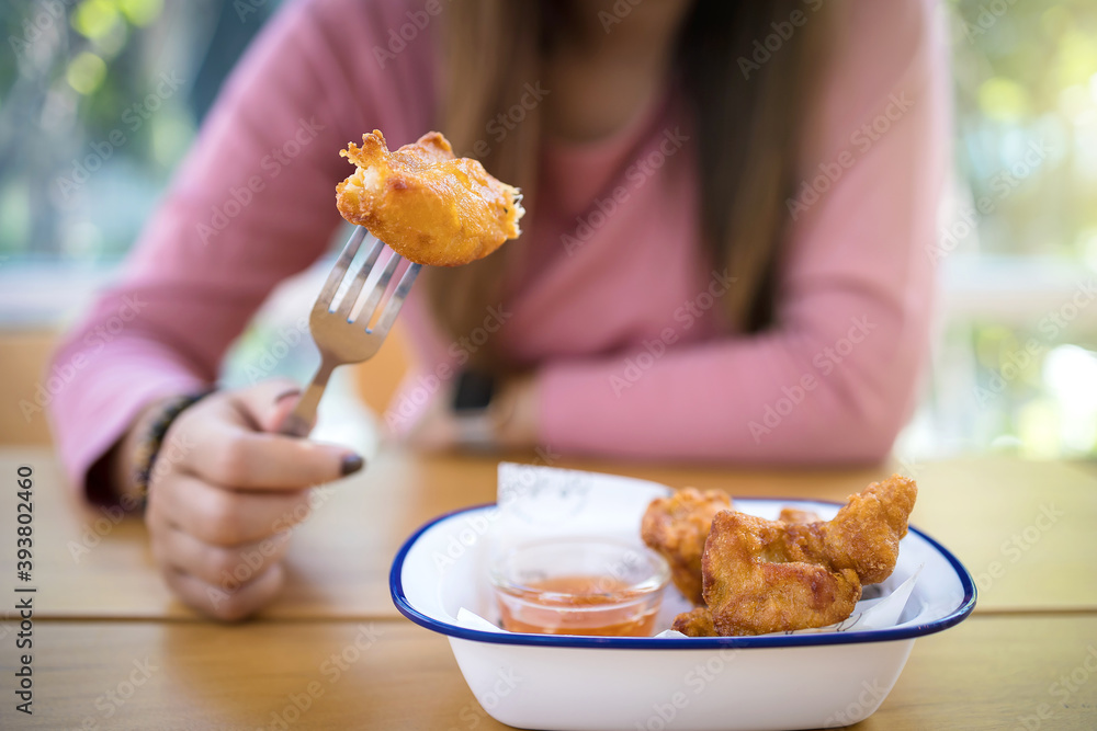 Asian woman eating fried chicken by fork on blurred background.