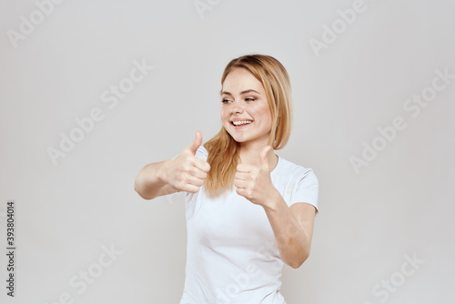 cheerful blonde in a white t-shirt gesturing with her hands light background