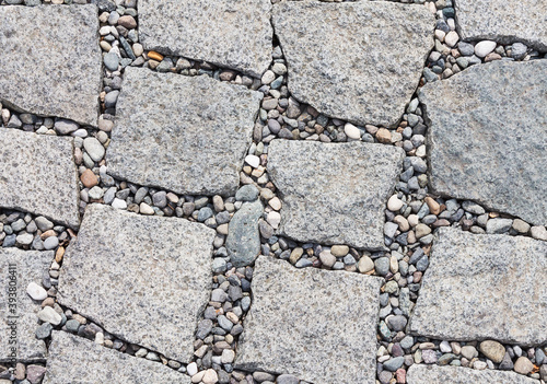 The pavement is made of stone in the form of slabs with uneven edges and pebbles between them. Textural abstract background for designers. photo