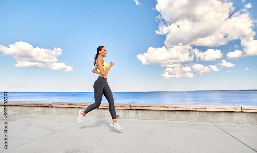 fitness, sport and healthy lifestyle concept - young woman running along sea promenade