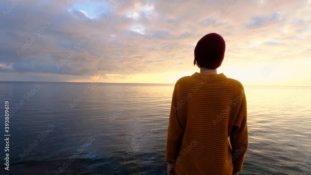 Woman wearing a yellow sweater and a red hat and enjoying beautiful colorful sunset above sea from cape. concepts of the winner, freedom, happiness. hiker exploring nature Woman wearing a yellow sweater and a red hat and enjoying beautiful colorful sunset above sea from cape. concepts of the winner, freedom, happiness. hiker exploring nature