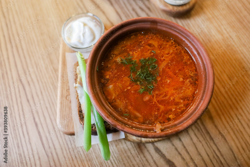 Ukrainian borscht with bacon bread sour cream and herbs on a wooden table in the dining room Ukrainian borscht with bacon bread sour cream and herbs on a wooden table in the dining room