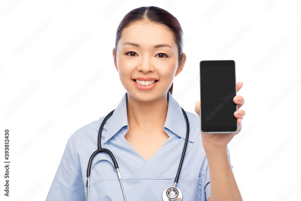 medicine, profession and healthcare concept - happy smiling asian female doctor or nurse in blue uniform with stethoscope showing smartphone over white background medicine, profession and healthcare concept - happy smiling asian female doctor or nurse in blue uniform with stethoscope showing smartphone over white background