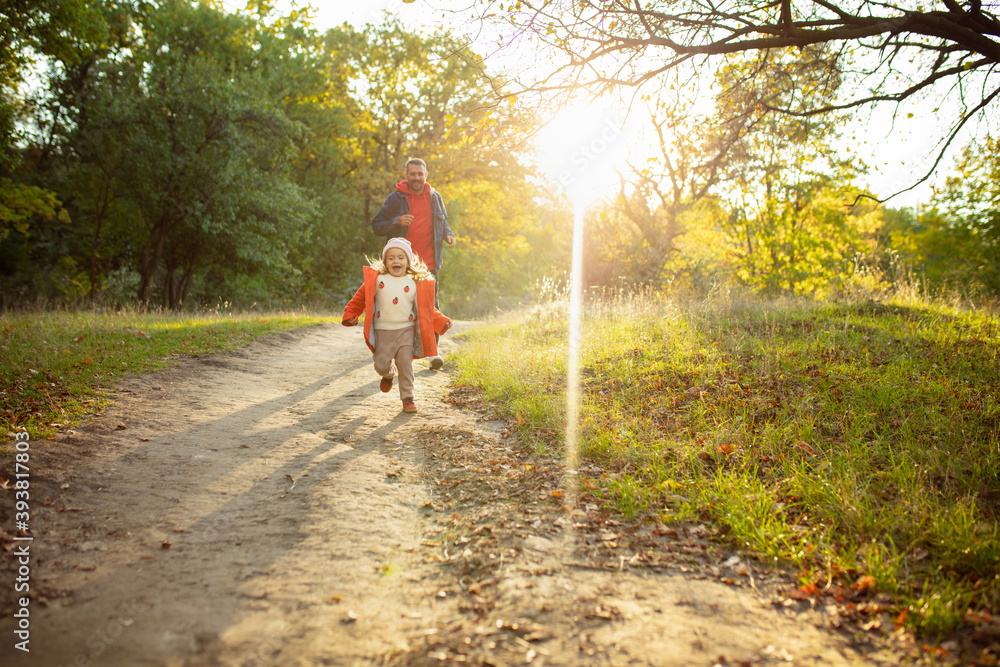 Obraz premium Sunshine. Happy father and little cute daughter walking down the forest path in autumn sunny day. Family time, togehterness, parenting and happy childhood concept. Weekend together with sincere