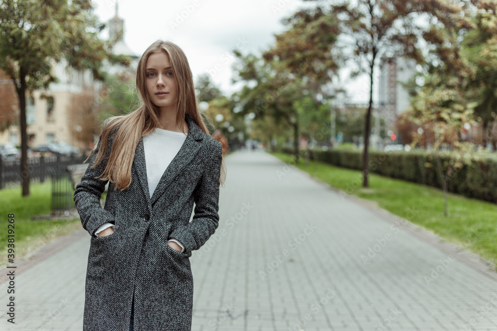 pretty woman in grey wool coat standing on the alley and looking in the camera pretty woman in grey wool coat standing on the alley and looking in the camera
