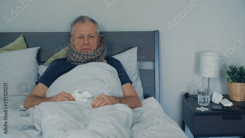 A sick man is lying in bed and coughs and has a runny nose.