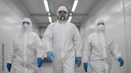 Team of virologists in hazmat suits walking in corridor to do disinfection photo