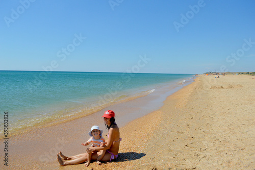 Fototapeta Naklejka Na Ścianę i Meble -  Mom and baby sit on a sandy beach near the black sea on a clear, Sunny day.