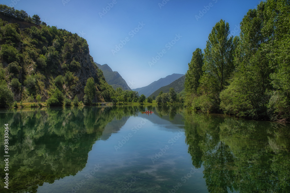 Lake with large green trees and a blue sky with reflections on the water
