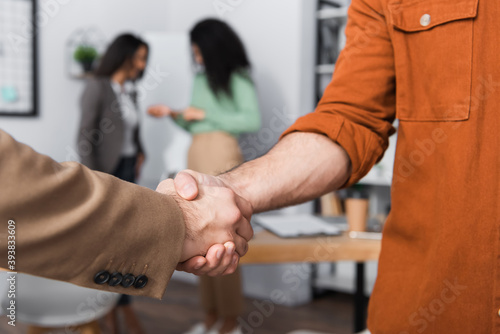 hispanic businessmen shaking hands near businesswomen on blurred background