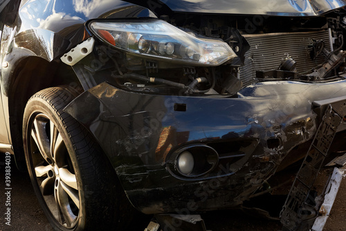 A close-up of the front of a black car destroyed in an accident.