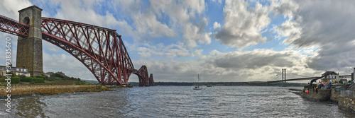 The original Forth Rail Bridge and the newer Forth Road Bridge stretch side by side from the harbor at North Queensferry across the Firth of Forth towards Edinburgh.