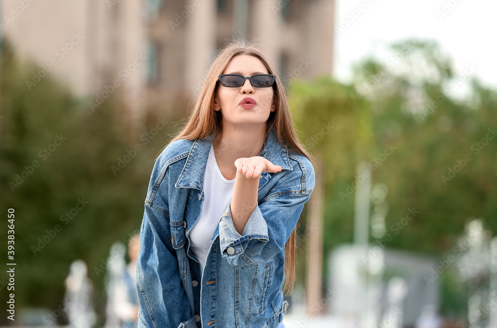 Beautiful woman with stylish sunglasses blowing kiss outdoors