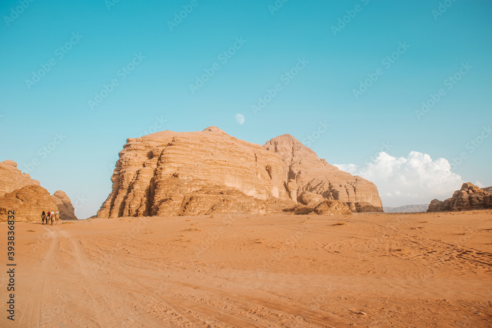 People on camels pass the sand dunes in the desert, which is surrounded by stone rocks and pink sand, animals walk without getting tired,there is not enough water, and the hot hot sun burns everything People on camels pass the sand dunes in the desert, which is surrounded by stone rocks and pink sand, animals walk without getting tired,there is not enough water, and the hot hot sun burns everything