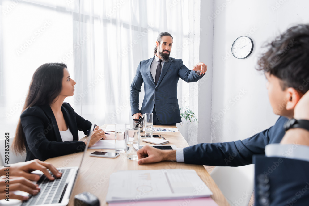 Confident hispanic executive pointing with finger at co-worker during business meeting in office on blurred foreground Confident hispanic executive pointing with finger at co-worker during business meeting in office on blurred foreground