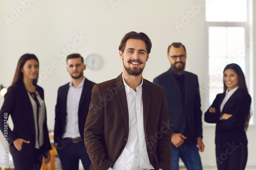 Smiling businessman or company owner looking at camera over positive colleagues at background