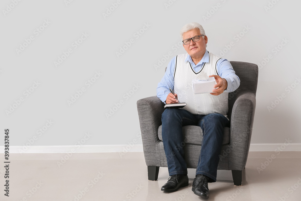 Male psychologist sitting in armchair near light wall