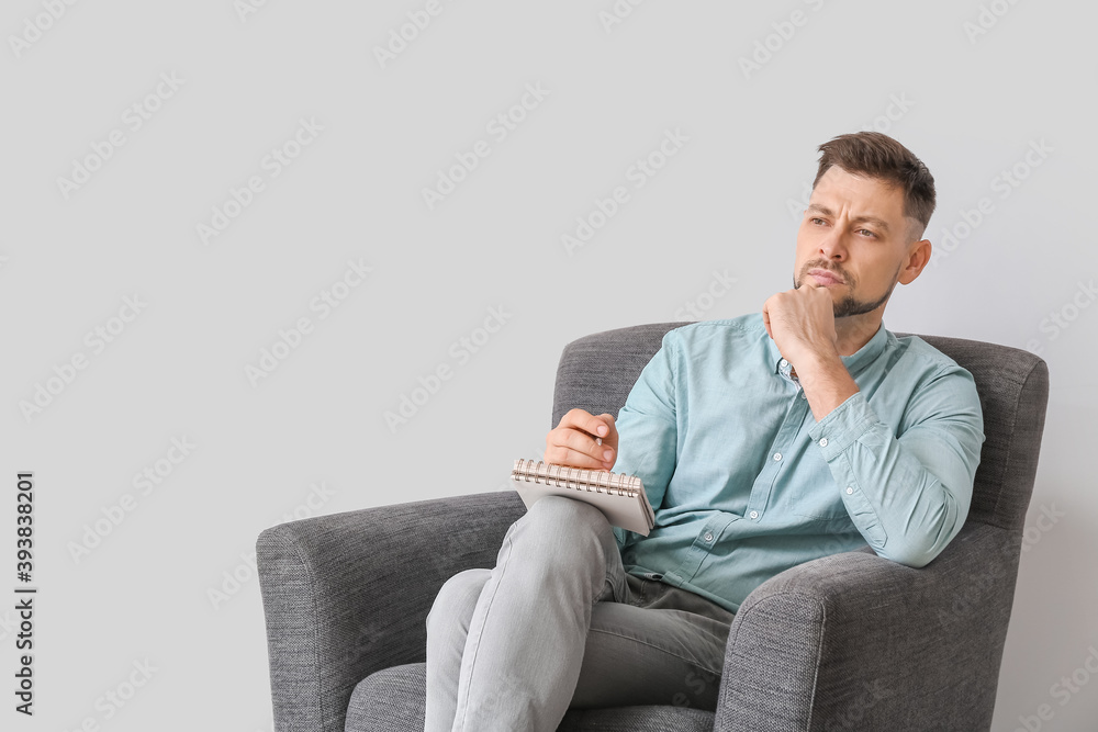 Male psychologist sitting in armchair on light background