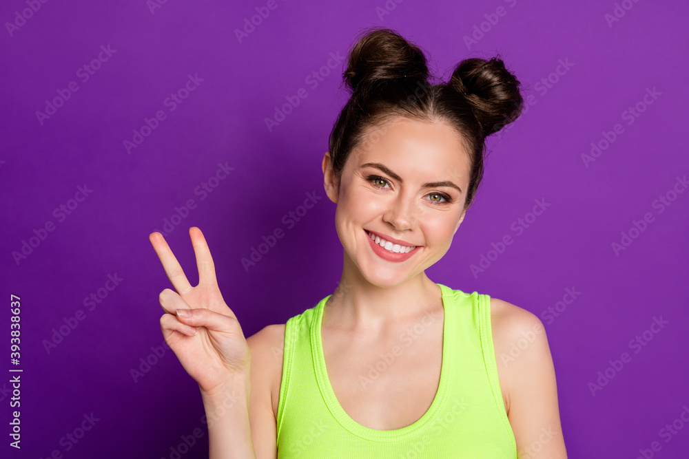 Attractive lady two funny buns showing v-sign symbol wear green singlet isolated violet color background Attractive lady two funny buns showing v-sign symbol wear green singlet isolated violet color background