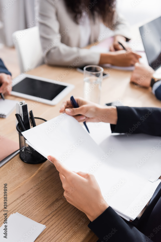 Cropped view of businesswoman working with documents near colleagues and devices on blurred background Cropped view of businesswoman working with documents near colleagues and devices on blurred background